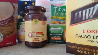 Dons de denrées alimentaires pour l'opération Martigues Solidaire posé sur une table avec affiche de l'édition 2024. Pâtes, jus de fruits, confitures, savons et brosse à dent sont représentés sur la photo