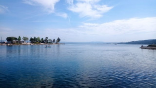 Etang de Berre et sa vaste étendu d'eau avec des arbres sur ses abords et un kayak qui glisse sur l'eau. Les nuages dans le ciel amène un aspect paisible à la photo