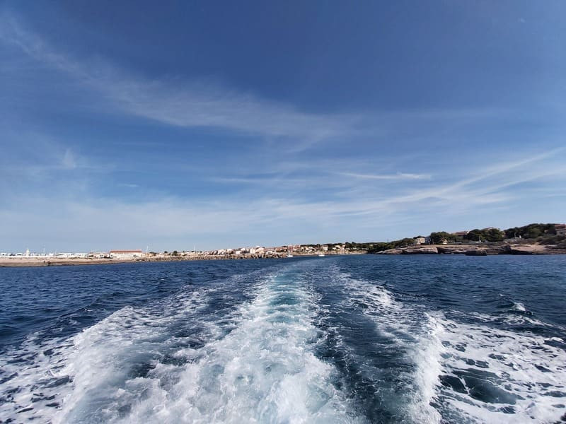 Trainée de vagues laissé par un bateau en mer méditerranée qui va en direction des calanques de la Côte Bleue. Au loin, le port de Carro et ses maisons typiques sont visibles sur la côte