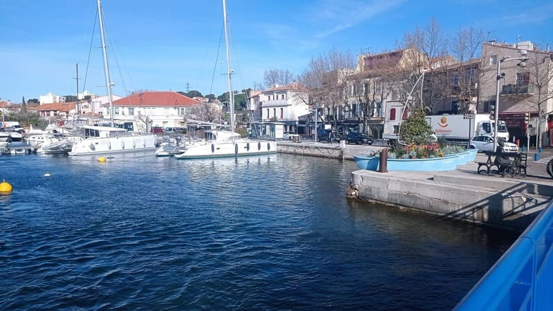 Vue générale du quartier de Ferrière prise depuis l'un des deux ponts bleus de Martigues. On y voit les voiliers amarrés sur le port, les bâtiments du centre-ville et les barques en fleurs, symbole du quartier