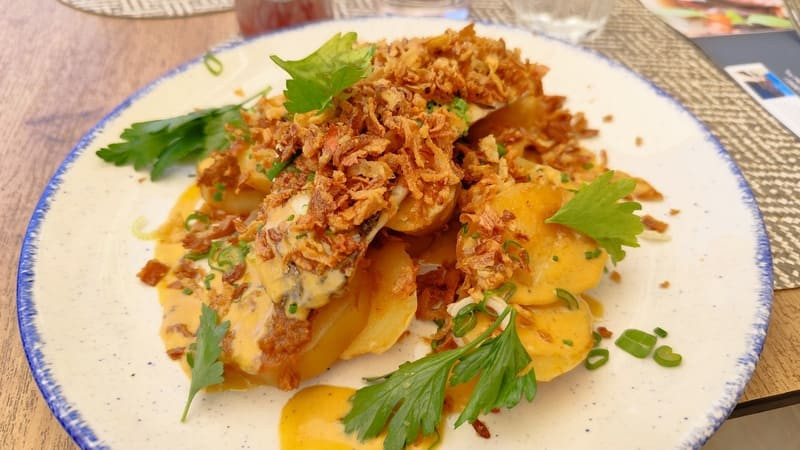 Assiette blanche aux contours bleus avec un poisson soupoudré d'oignons confits et pommes de terre à l'ancienne. Posé sur une table en bois, le plat est traditionnel