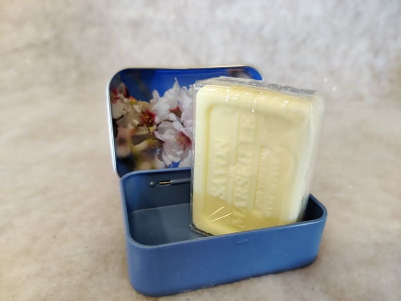 Savon de Marseille de la marque Esprit Provence à l'amande douce dans sa jolie boîte avec image de fleurs d'amandier. La boîte est bleue posée sur une surface blanche qui fait ressortir sa couleur éclatante