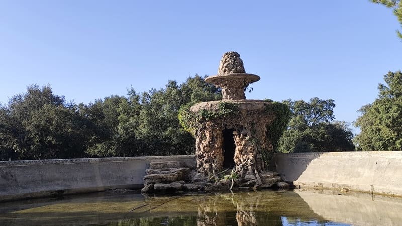 Un gran estanque de piedra, medio lleno, con su manantial aún visible. La hierba silvestre ha invadido la zona y adorna las piedras del monumento visible en el centro del Gran Parq - © Otmartigues / MyriamF