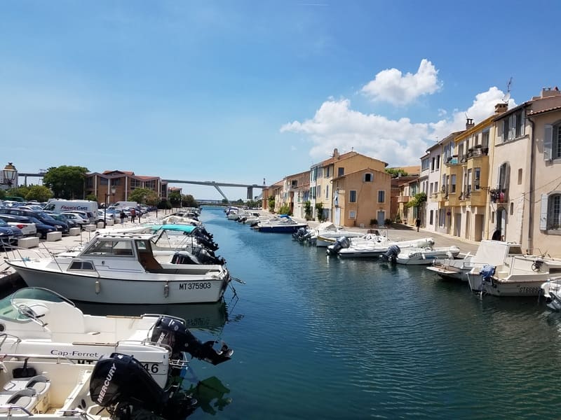Canal qui coupe le quartier de l'Ile en deux. De part et d'autres, des bateaux à moteurs amarrés. Un pont bleu traverse le canal pour les passants. Au loin, le viaduc autoroutier.  - © Otmartigues / MyriamF
