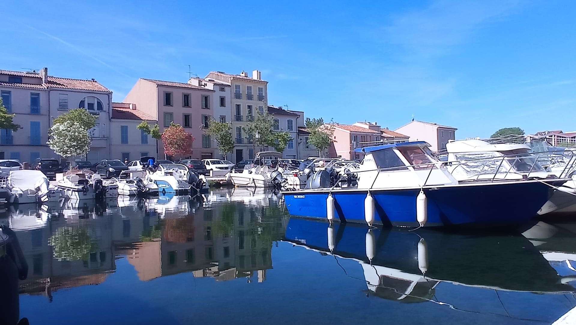 Façades colorées du centre-ville de Martigues en arrière plan. Bateaux à moteurs amarrés sur le quai au coeur du quartier de l'Ile. Leurs reflets dans l'eau calme donne un air paisible - © Otmartigues / MyriamF