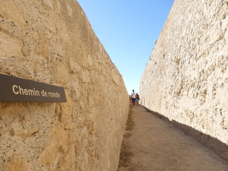 Photo taken from above of the Fort de Bouc patrol path, indicated by a sign. Participants in the tour, visible in the distance, can access it and discover this unique part of Fort  - © Otmartigues / KarimK