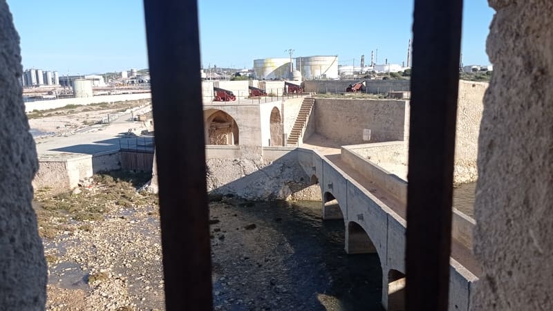 Bars mit Blick auf den Innenhof des Fort de Bouc, das an seine Rolle als Staatsgefängnis im Mittelalter erinnert. In der Ferne sind Treppen und Kanonen inmitten eines Industriegebi - © Otmartigues / MyriamF