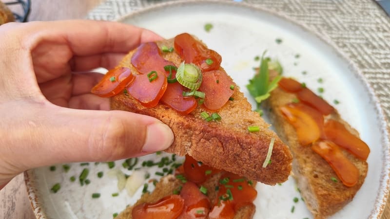 A hand holds a bottarga sandwich. Thick bread dipped in oil, butter, and strips of bottarga for a gourmet tasting in Martigues - © Otmartigues / MyriamF