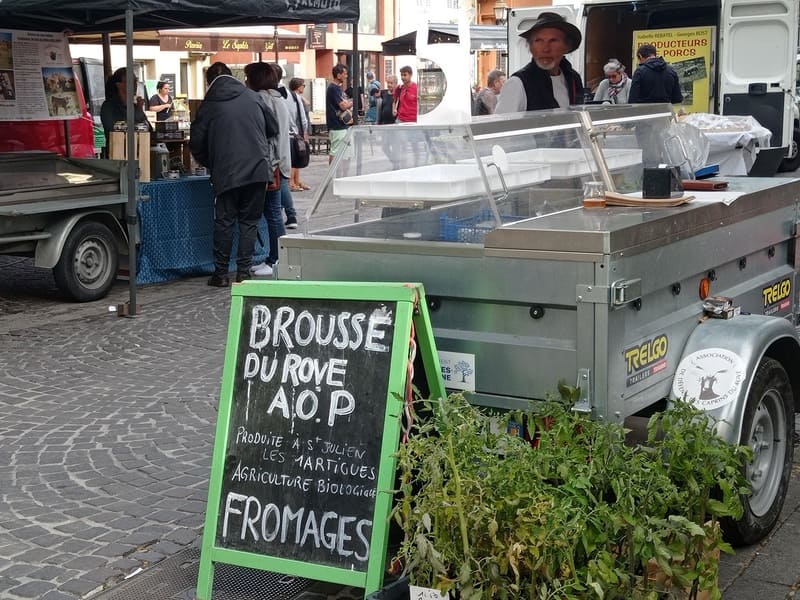 Local producers' market every Tuesday in Martigues. A sign in the foreground advertises the sale of Brousse du Rove AOP and goat cheeses from a local producer. - © Otmartigues / MyriamF