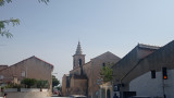 Vue sur le village de la Couronne depuis son entrée. Le clocher de l'église Saint-Jean Baptiste domine les maisons environnantes. Une grande rue travers le village sur laquelle circule une voiture rouge.
