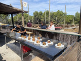 L'équipe de Aïoli Caganis et les participants de l'atelier cuisine à la ferme préparent des hamburgers avec des produits frais de la ferme. Les hamburgers sont posés dans des assiettes sur un plan de travail tandis que les participants regardent le chef 