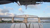 Photo prise depuis un bateau, on voit l'arrière du bateau et le pont de Caronte avec des nuages dans le ciel