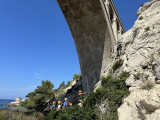 Le groupe de participant porte des casques de sécurité. Ils sont regroupées sous un pont de Carry-le-Rouet. La végétation auprès de la calanque est dense