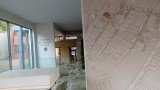 Vue de l'intérieur de la vitrine archéologique du quartier de l'Ile. Un plan représentatif des habitations (dessin) et des vestiges en pierre.