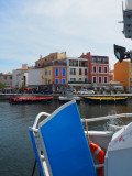 A l'arrière du bateau bleu, une bouée de sauvetage au premier plan. Au second pla, les barques rouges et jaunes des barques traditionnelles des rameurs vénitiens et les maisons colorées.