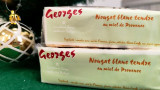 Deux paquets de nougats blanc au miel sont posés l'un sur l'autre avec l'étiquette de l'apiculteur visible sur l'emballage. Du nougat tendre au miel de Provence proposé par Georges.