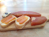 Whole bottarga on a wooden board with slices of bread topped with thin slices of bottarga for tasting