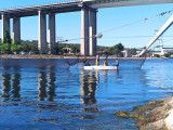 Distant view of the three fishermen on their boat in the canal, with the highway viaduct in the background and nets set up for mullet fishing