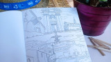Carnet de coloriage ouvert avec un dessin d'une fontaine emblématique de Martigues, accompagné d'un chapeau de paille et de crayons de couleur
