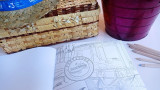 Carnet de coloriage ouvert avec un dessin coloré et des crayons de couleur à côté, présenté avec une boîte tissée