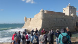 Groupe de personne devant le Fort de Bouc vu de côté. Il est en contre-bas, les vagues de la mer méditerannée déferlent sur son flanc.