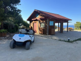 White golf cart with the Camping Paradis logo on the front side, open without a hood. Wooden building with Camping Paradis set with Tom's golf cart on display during the Martigues open house.