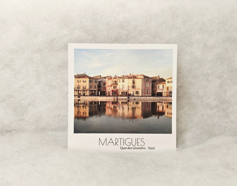 Postal cuadrada que muestra las coloridas fachadas provenzales reflejadas en el canal, en el distrito de Tessé, Martigues. - © Otmartigues / MarianneB Postal vintage de Martigues que muestra las coloridas fachadas del Quai des Girondins, en el distrito de Tessé. Destaca los reflejos simétricos de los edificios amarillos y ocres en el agua del canal