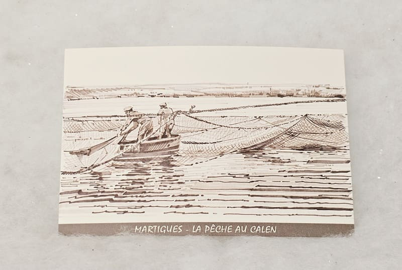 A gray and white postcard depicting traditional fishing at the Calen pond, still practiced in Martigues. This postcard is available exclusively at the Martigues Tourist Office.