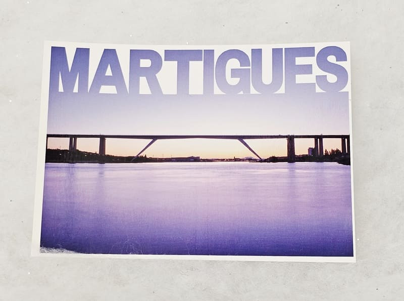Postal que muestra la ciudad de Martigues en el cielo sobre el viaducto de la autopista, a contraluz al atardecer. La foto es predominantemente azul medianoche, un contraste entre el cielo y el mar. - © Otmartigues / MarianneB Postal fotográfica que muestra el viaducto de la autopista al atardecer, símbolo de Martigues. Postal a la venta en la Oficina de Turismo de Martigues