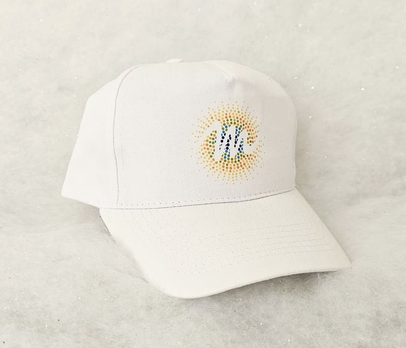 Gorra blanca con el logotipo M de la Oficina de Turismo de Martigues. La M está escrita con un patrón ondulado, trazando la letra dentro de un sol de colores que se difumina del azul al amarillo. - © Otmartigues / MarianneB Gorra blanca con el logotipo M de Martigues, de la gama Sun, en colores del arcoíris. Exclusiva de la Oficina de Turismo de Martigues.