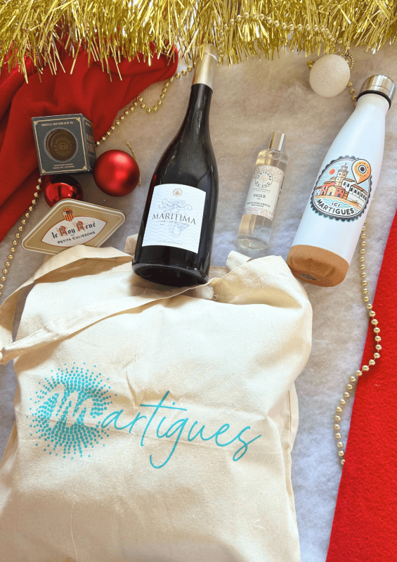 Christmas Gift Set with a Bottle of Red Wine is available at the Martigues Tourist Office shop. - © Otmartigues / PaolaM A Christmas gift set is available at the Martigues Tourist Office, including a Martigues tote bag and water bottle, a bottle of Maritima red wine, a Marius Fabre soap, a box of Roy René calissons, and