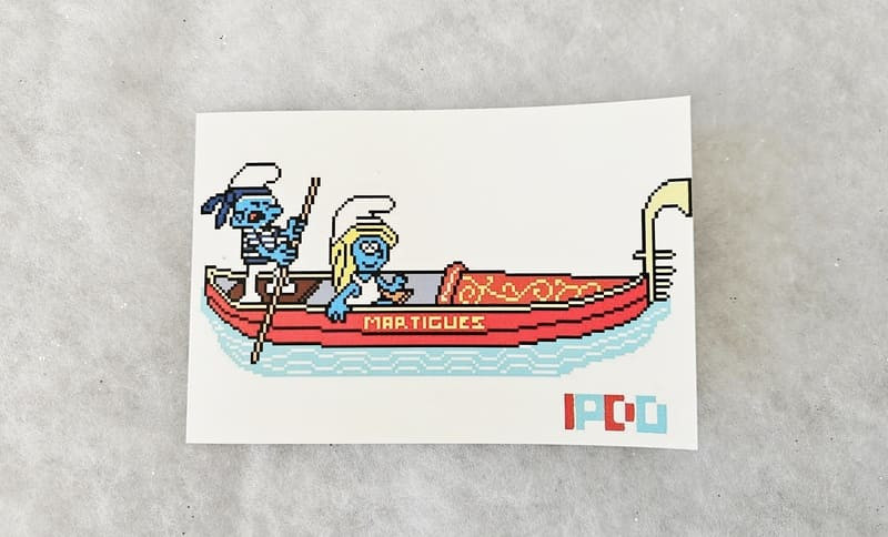 Postal de IPDO con un Pitufo y una Pitufina en una góndola, un guiño a Martigues, la Venecia de la Provenza. - © Otmartigues / MarianneB Postal de La Góndola con los Pitufos en un mosaico, ubicada en el centro de Martigues. Una creación original de IPDO, disponible en la tienda de la Oficina de Turismo de Martigues.