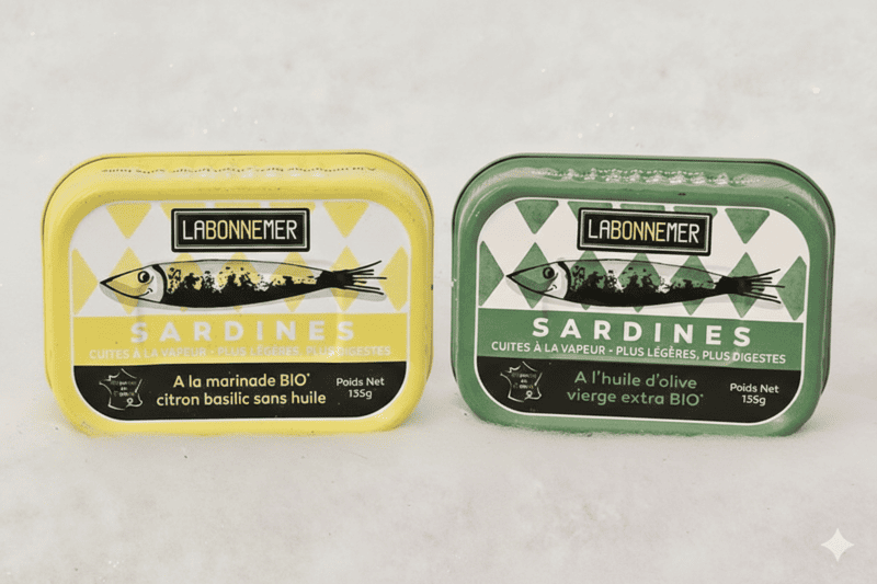 Zwei Dosen Sardinen in Olivenöl, eine grüne und eine gelbe, mit dem Schriftzug „La Bonne Mer“ (Das gute Meer) und einem Sardinenmotiv. - © Crédit photo : Otmartigues-MarianneB / Montage : IA Gemini Bio-Sardinen in Olivenöl, hergestellt in der Konservenfabrik Ferrigno. Erhältlich im Tourismusbüro von Martigues.