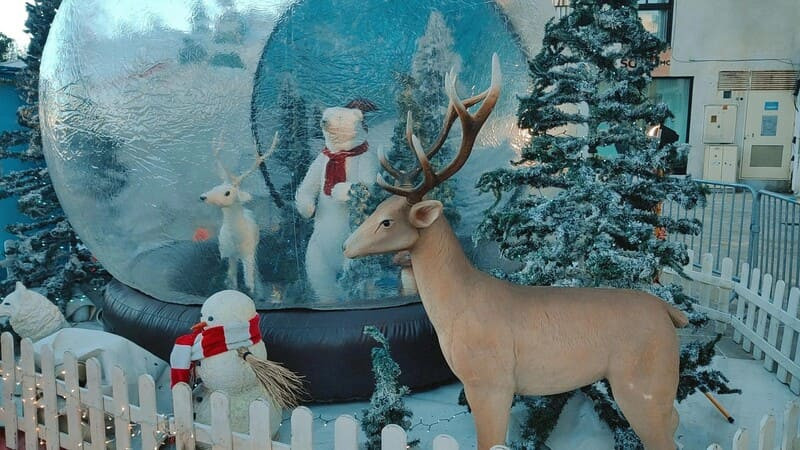 Christmas decoration featuring a glowing reindeer, polar bear, and snowman on a blue background, surrounded by festive trees and barriers