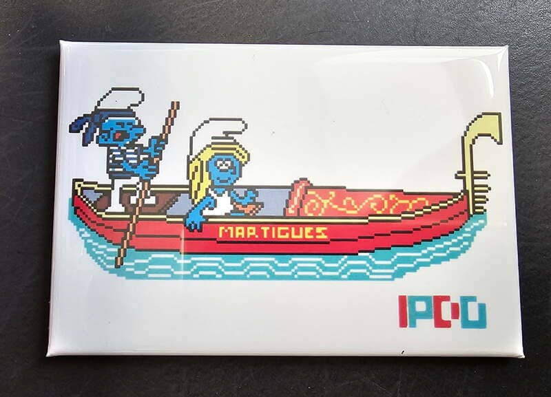 Magnet mit einem Schlumpf und einer Schlumpfine in einer Gondel und der Aufschrift „Martigues“, die auf ein IPDO-Mosaik im Stadtzentrum verweist.