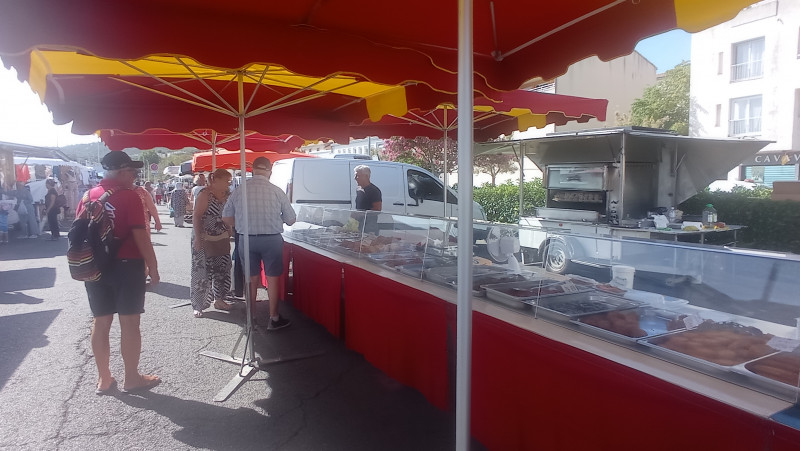 Etal du marché de Jonquières à Martigues de poulet rôti et d'accompagnements typique de Provence tels que les beignets de courgettes. L'étal est rouge, il a des parasols rouges et jaunes pour protéger du soleil.