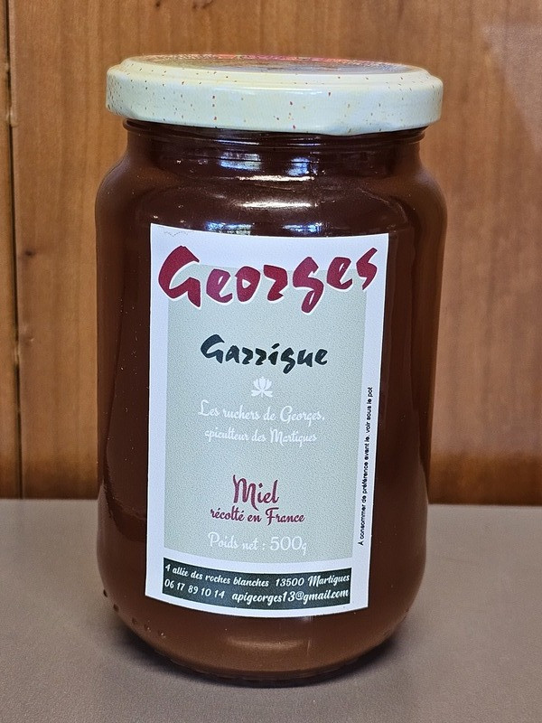 500-g-Glas Honig von Ruchers de Georges, das Buschlandhonig mit einem holzfarbenen Hintergrund illustriert.