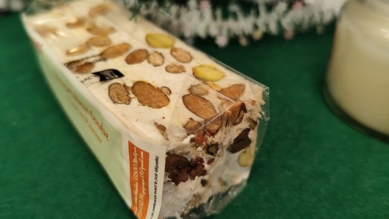 Les Ruchers de Georges - Nougat blanc au miel de Provence - © Otmartigues / MyriamF Un nougat blanc dans son emballage posé sur fond vert. Des gros morceaux d'amandes sont visibles, ce qui confère au produit son naturel et donne envie de croquer dedans