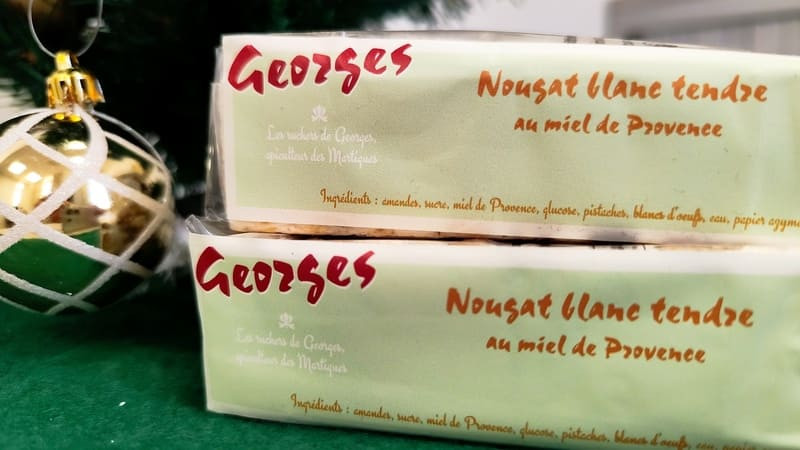 Les Ruchers de Georges - Nougat blanc au miel de Provence - © Otmartigues / MyriamF Deux paquets de nougats blanc au miel sont posés l'un sur l'autre avec l'étiquette de l'apiculteur visible sur l'emballage. Du nougat tendre au miel de Provence proposé par Georges.