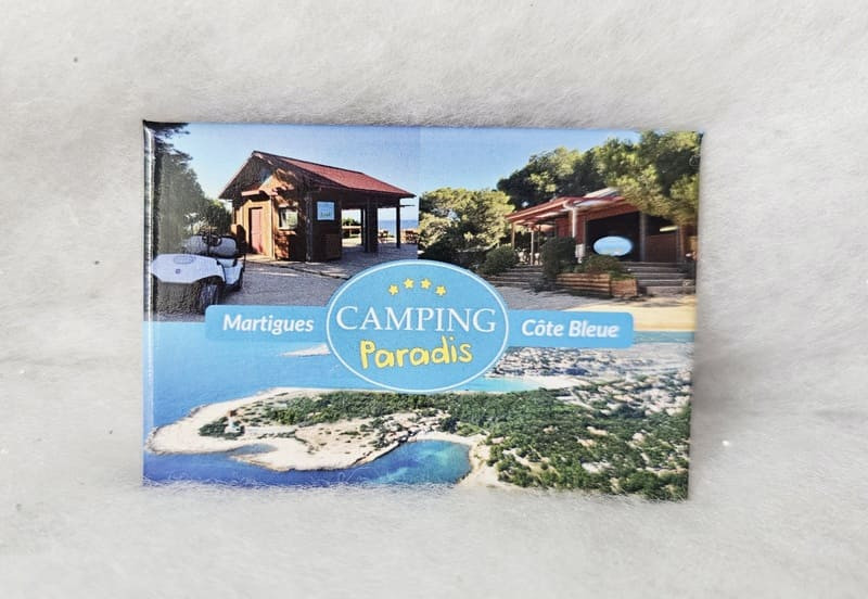 Magnet mit drei Fotos, darunter zwei mit Motiven aus der Camping Paradis-Serie im oberen Bereich. Darunter ein Luftbild der Côte Bleue. In der Mitte das Camping Paradis-Logo. - © Otmartigues / MarianneB Magnet mit Fotos vom Drehort von „Camping Paradis“ in La Couronne, Martigues. Exklusives Produkt im Sortiment des Tourismusbüros Martigues.