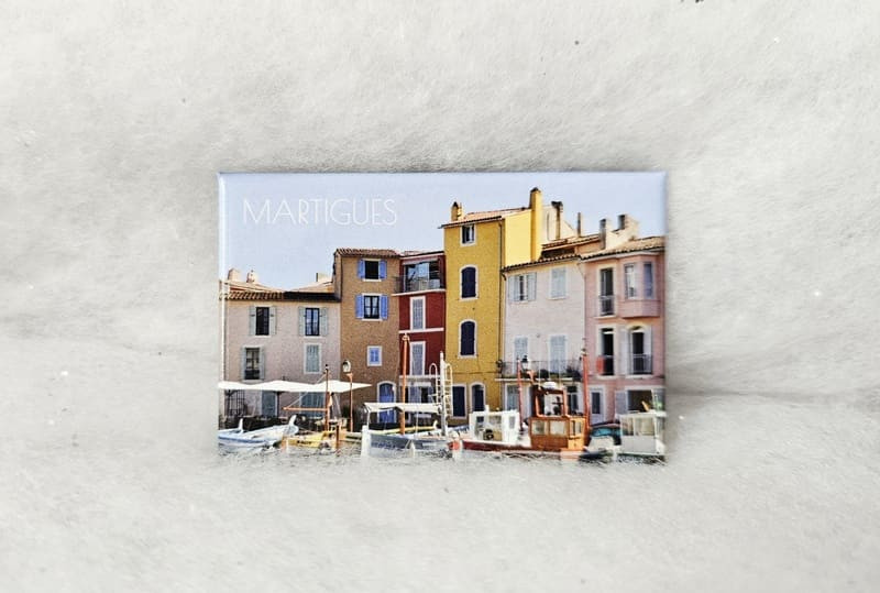 Imán rectangular con una foto en primer plano del Espejo de Pájaro. Primer plano de las coloridas fachadas y las cubiertas de las embarcaciones tradicionales. Martigues se menciona en la esquina super - © Otmartigues / MarianneB Imán que representa los coloridos barcos y casas del Espejo de Pájaro, una atracción turística de Martigues. Un regalo de recuerdo disponible en la Oficina de Turismo de Martigues.