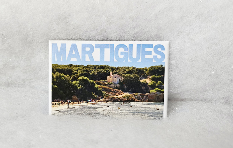 Imán con una foto de la capilla de Sainte-Croix, su verde ladera, su playa de arena fina y su mar cristalino. El nombre de Martigues aparece superpuesto en el cielo. - © Otmartigues / MarianneB Imán con una foto de la Playa de Sainte-Croix en la Costa Azul y su icónica capilla con vistas al paisaje. Imán exclusivo disponible en la Oficina de Turismo de Martigues