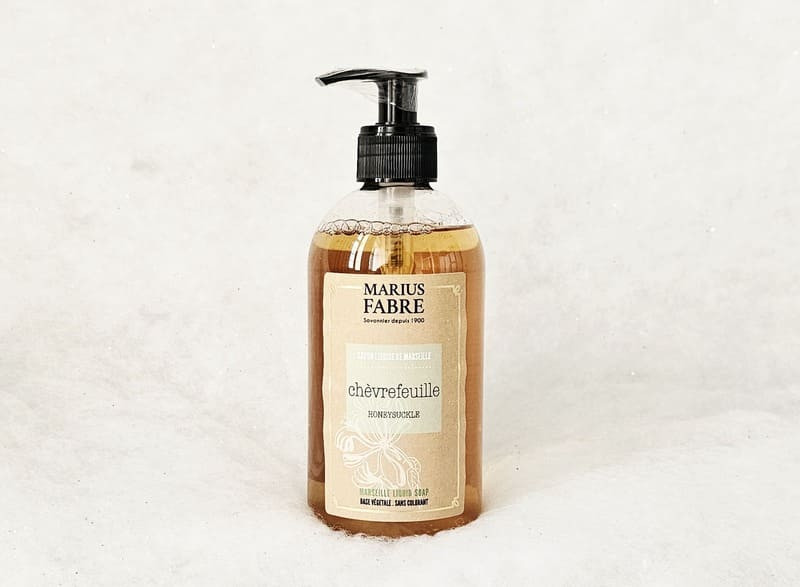 Jabón líquido en un envase de plástico transparente que revela su color marrón. Una etiqueta de elegante diseño cubre gran parte del frasco. Presenta el aroma a madreselva y la marca Marius Fabre. - © Otmartigues / MarianneB Jabón líquido de manos con aroma a madreselva de Marius Fabre. Disponible en la Oficina de Turismo de Martigues.