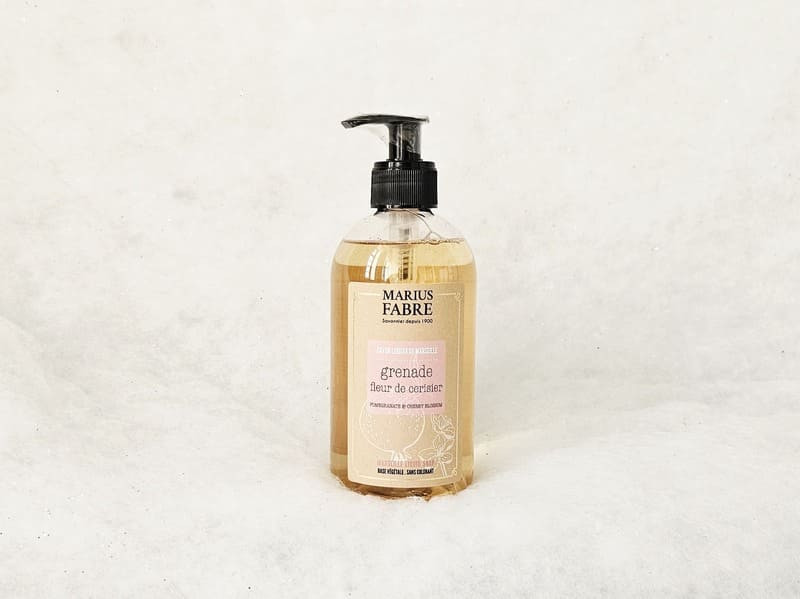Botella de jabón líquido de plástico transparente. Una etiqueta cubre la mayor parte de la superficie. Presenta la palabra granada sobre un fondo rosa y el nombre de la marca Marius Fabre. - © Otmartigues / MarianneB Jabón líquido Marius Fabre con aroma a granada y flor de cerezo, inspirado en el sur de Francia. Disponible en la Oficina de Turismo de Martigues.