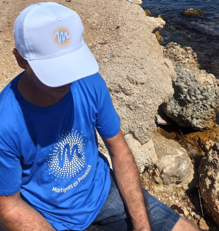 Man captured from above wearing a blue T-shirt and the white cap featuring the sun logo