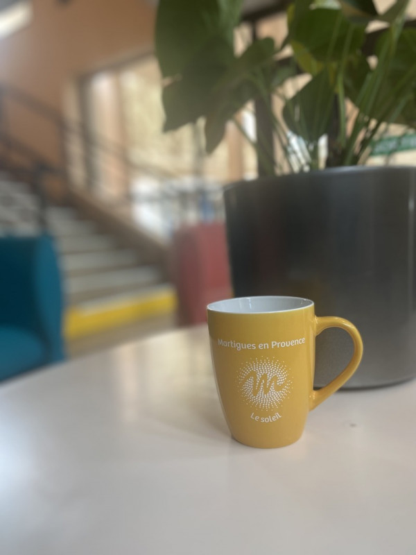 Leuchtende gelbe Tasse elegant auf einem grauen Tisch platziert, mit einer Pflanze im Hintergrund und einer verschwommenen Treppe, die der Szene Tiefe verleiht