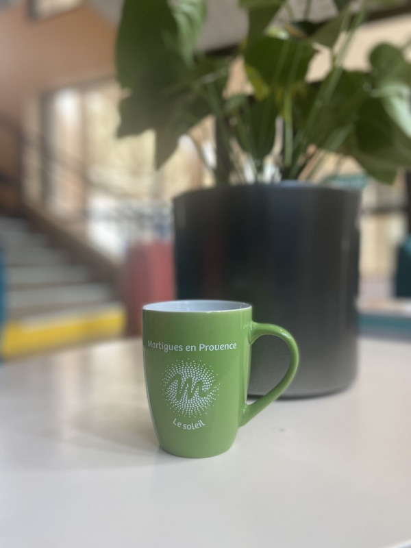 Bright green mug elegantly placed on a gray table, with a plant in the background and a blurred staircase adding depth to the scene
