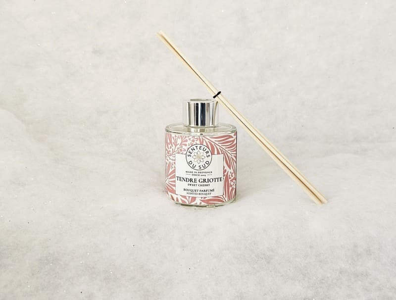 Ramo aromático con juncos de madera en la parte superior. La etiqueta roja con motivos florales cubre todo el envase de vidrio. Se indican la marca y la fragancia de Senteurs du Sud. - © Otmartigues / MarianneB Ramo aromático con aroma a guinda, creado por Senteurs du Sud. Una mezcla original de fragancias provenzales disponible en la Oficina de Turismo de Martigues.