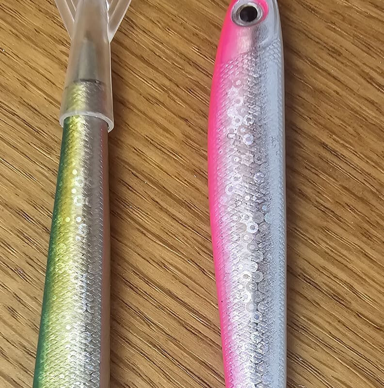 Two fish-shaped pens are placed on a table. The silver and glittery color, for children, is reminiscent of the local sardine in Martigues. The fish's tail diffuses the ink from the pen.