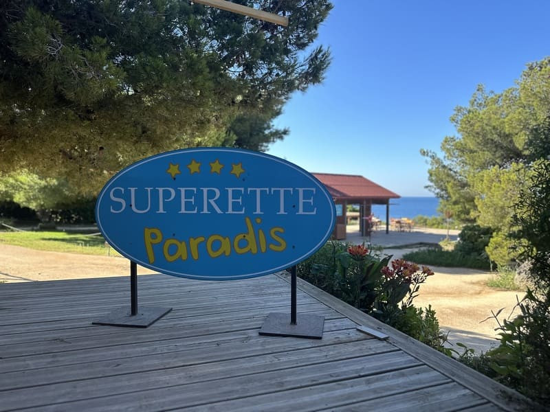 A sign in the series' colors, turquoise blue and yellow, with the words Sign for the entrance to the mini-market, as seen in the TF1 series Camping Paradis. See it during the open house at La Couronne, Martigues